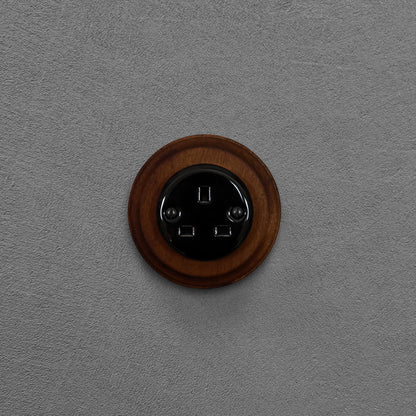 Black porcelain UK Plug Socket with dark wood frame, flush-mounted